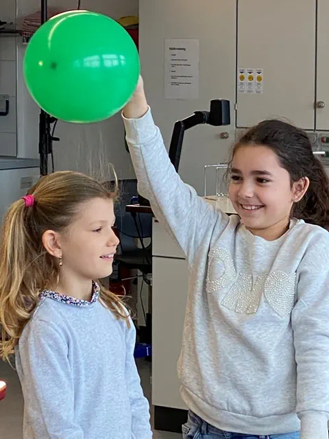 Einer Schlerin stehen die Haare zu Berge, weil sie ein Luftballon statisch aufgeladen hat