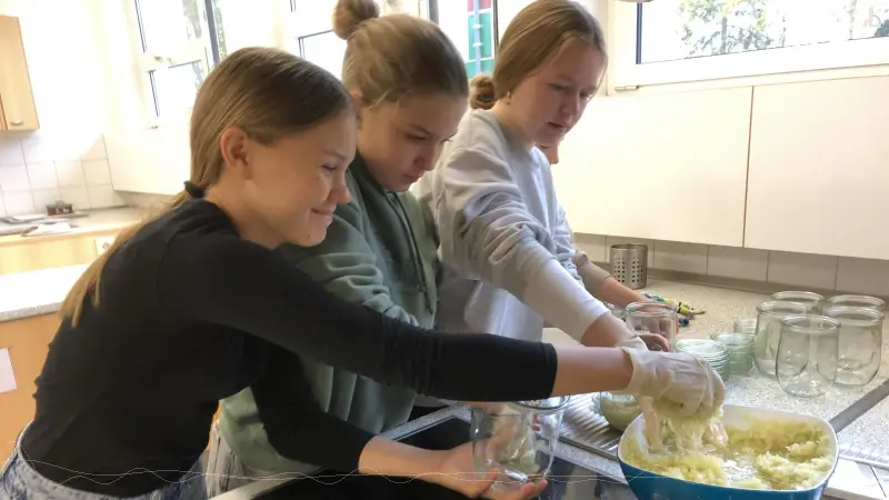 Drei Mdels befllen Einmachglser mit Kraut